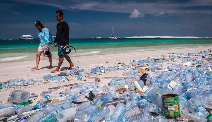 hình ảnh cặp đôi đi trên biển với đầy chai nhựa được vứt lung tung